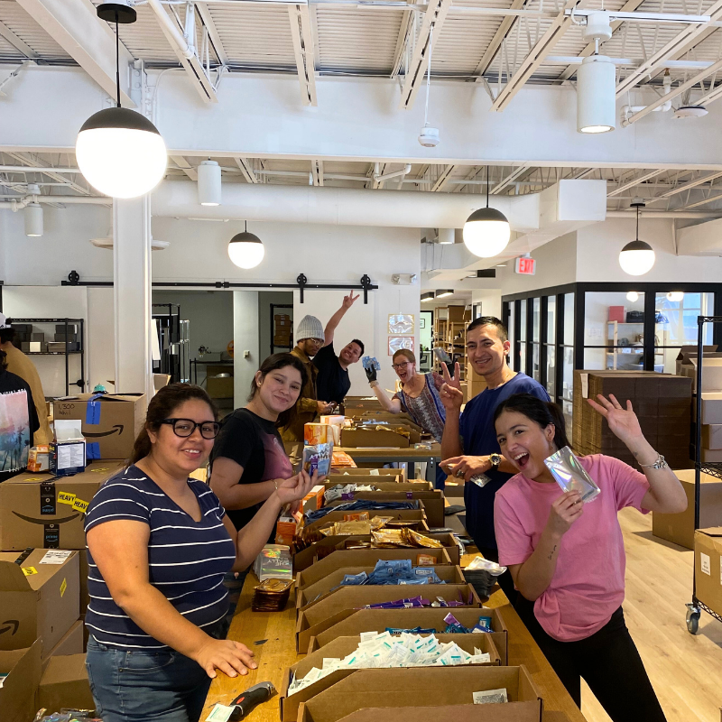 Sidekick Kitting team packaging orders in the warehouse, smiling happily for the camera